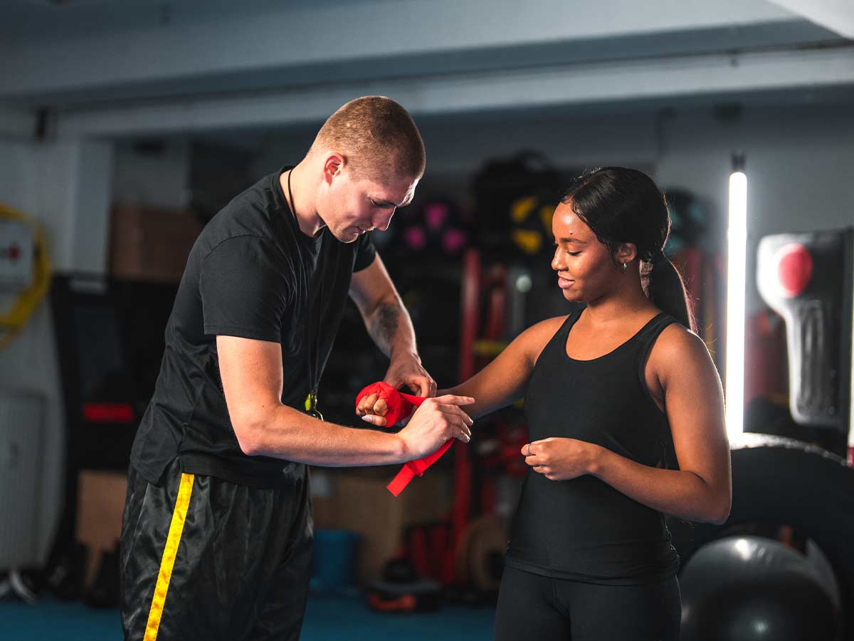 A male trainer wraps a female student's hands in preparation for training kickboxing.