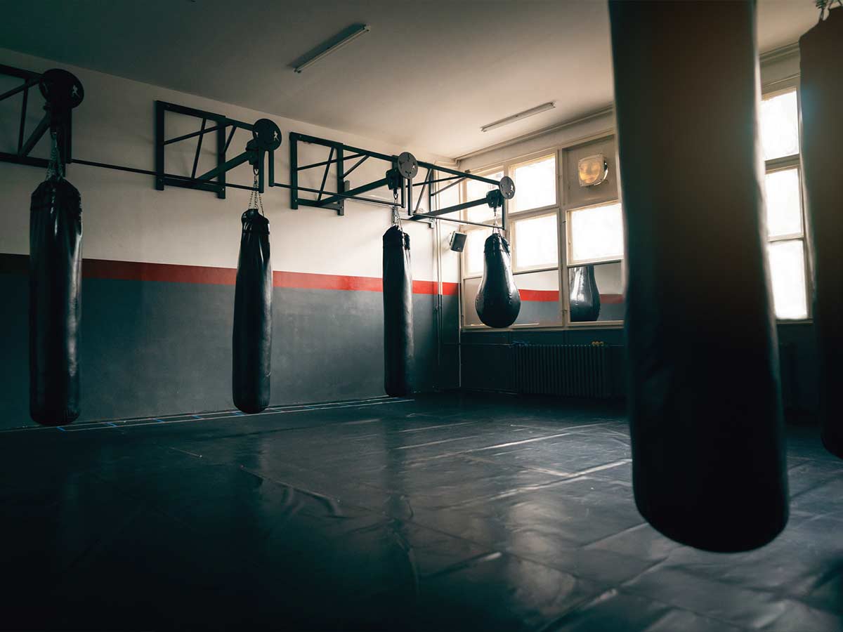 An empty martial arts gym with black floor and various punching bags hanging from the walls.