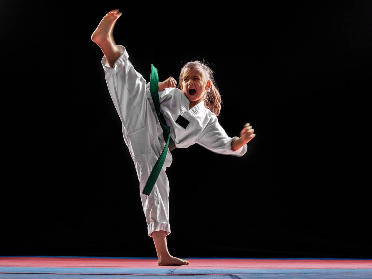 A young girl in a white robe does a high, taekwondo kick.