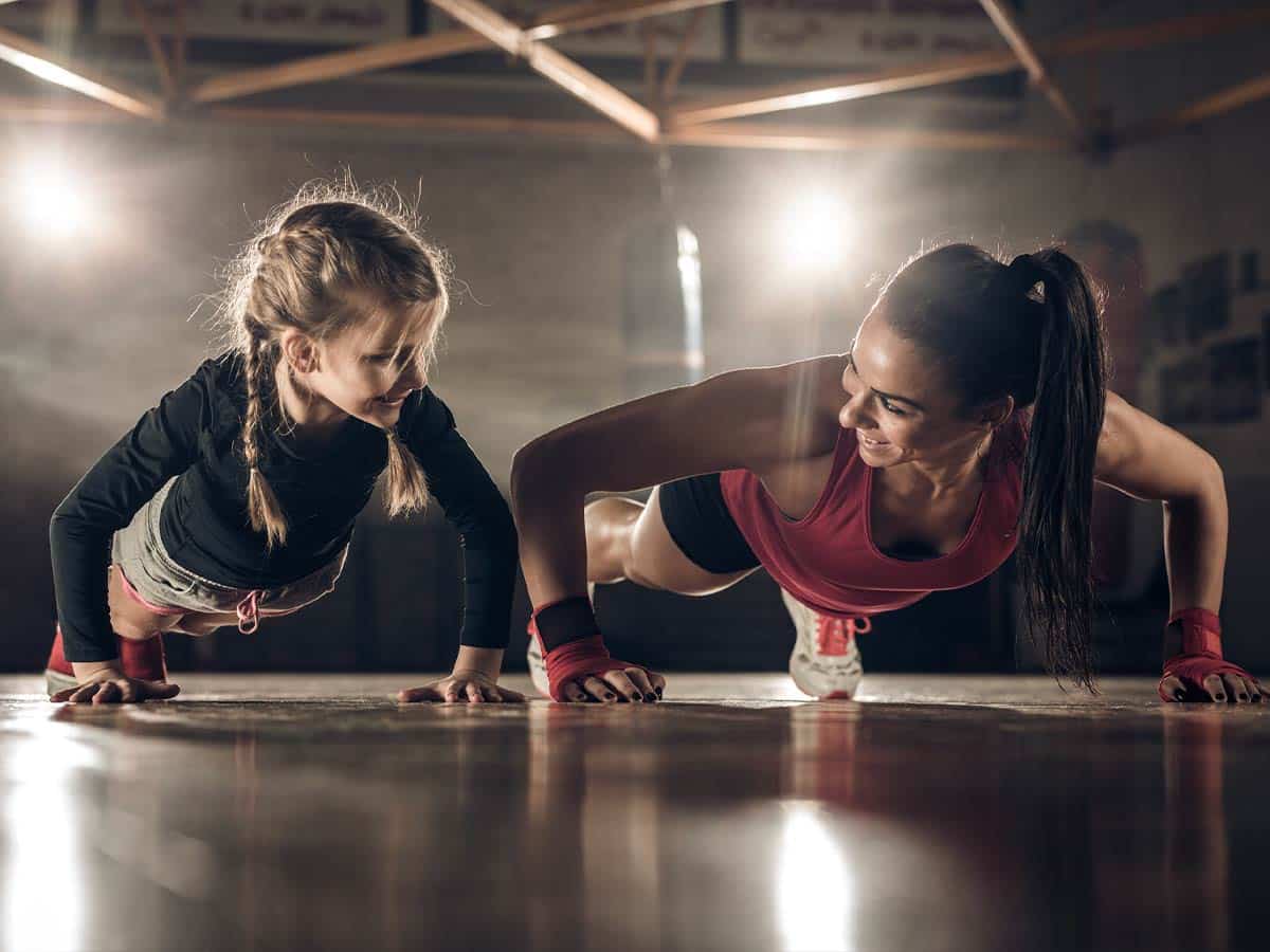 A female instructor does push ups next to a young martial arts student.