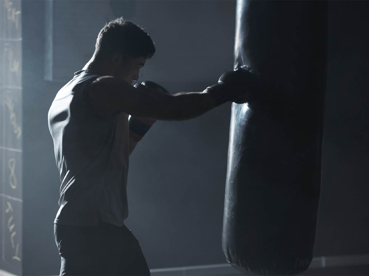 A muscular man wearing boxing gloves hits a punching bag as he trains for martial arts.