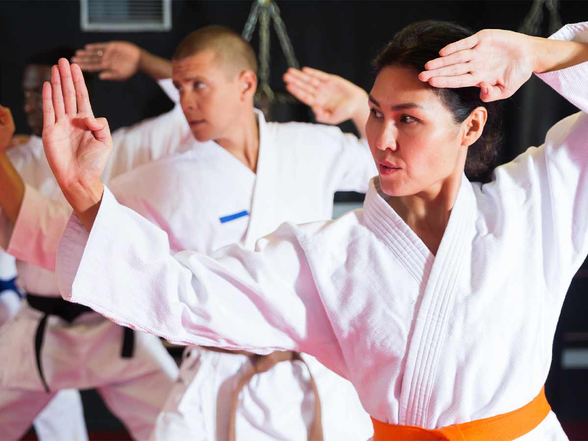 An Asian woman wearing an orange belt is in focus alongside a group of people training martial arts in Parksville.